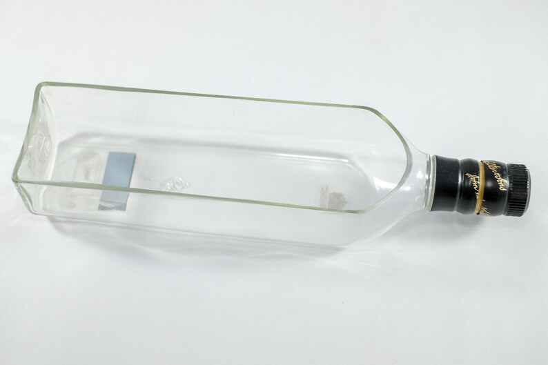 Puede incluir: Una botella de vidrio transparente con una tapa negra y letras doradas. La botella est&aacute; vac&iacute;a y se ha reutilizado como un plato decorativo.