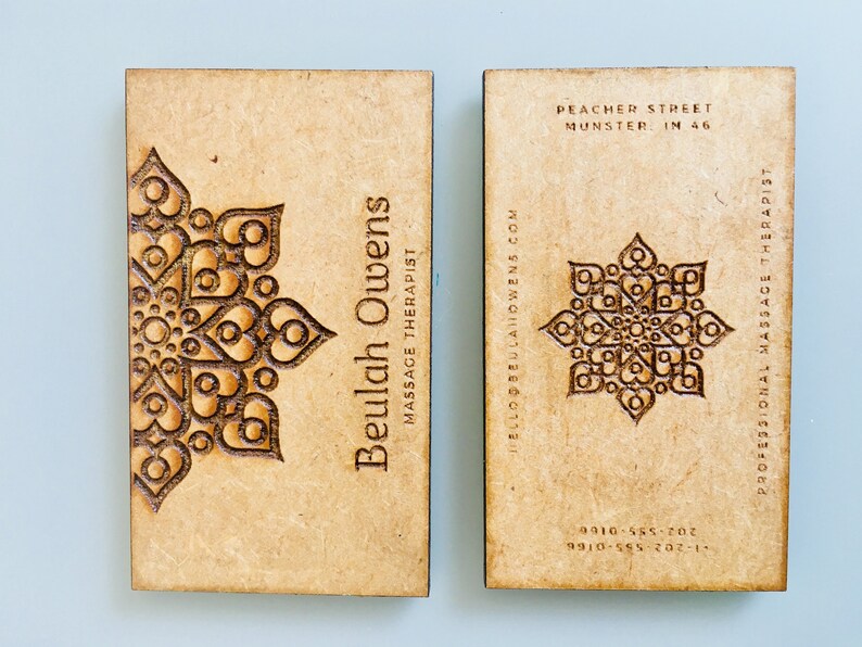 Op de afbeelding: Twee houten visitekaartjes met een decoratief ontwerp. De linker kaart heeft de tekst "Beulah Owens Massage Therapist" en een websiteadres. De rechter kaart heeft de tekst "Professional Massage Therapist", een adres en twee telefoonnummers.