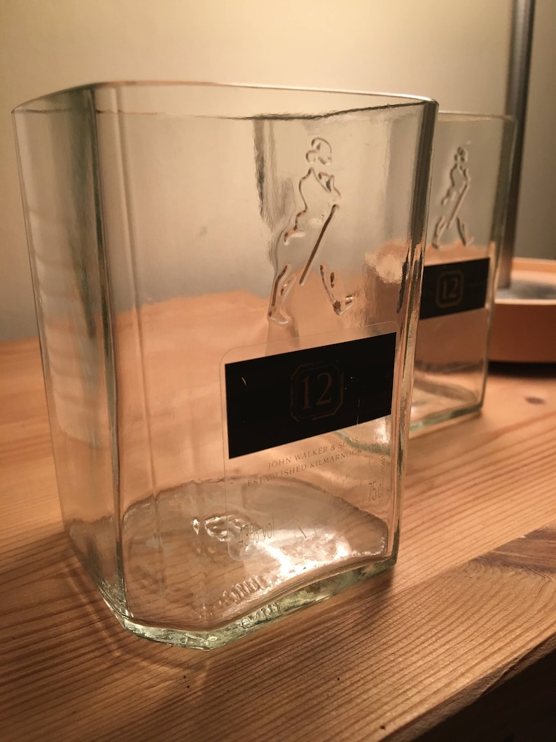 Op de afbeelding: Twee doorzichtige glazen flessen met een getextureerd oppervlak. De flessen zijn leeg en hebben een etiket met de tekst "John Walker & Sons" en "12" erop.