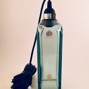May include: A clear glass bottle pendant light with a black cord and a black socket. The bottle has a gold label with the text "ESTABLISHED 1820".