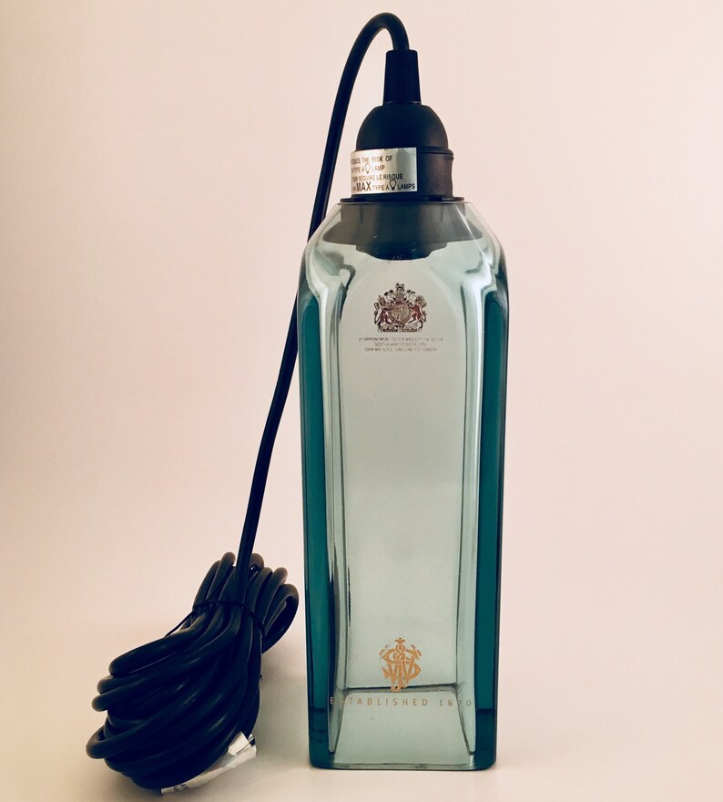 May include: A clear glass bottle pendant light with a black cord and a black socket. The bottle has a gold label with the text "ESTABLISHED 1820".