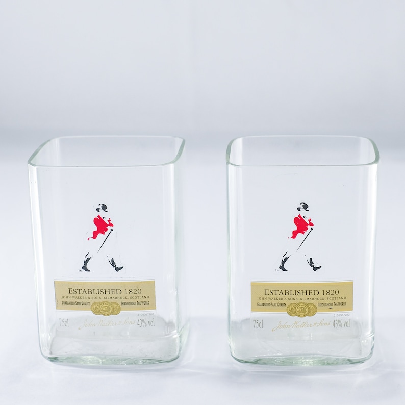 May include: Two clear glass tumblers with a square base. Each glass has a black and white image of a man in a red coat walking with a cane. The text "Established 1820" is printed on each glass.