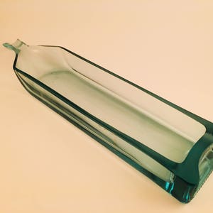 May include: A clear glass bottle with a rectangular shape, cut to create a decorative dish. The bottle is light green in color.