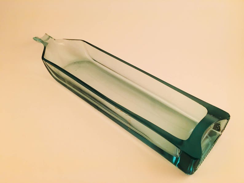 May include: A clear glass bottle with a rectangular shape, cut to create a decorative dish. The bottle is light green in color.