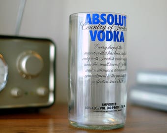 May include: A clear glass bottle of Absolut Vodka, with a blue label and white text. The label reads "Absolut Country of Sweden Vodka". The bottle is sitting on a wooden surface.