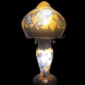 May include: A vintage table lamp with a yellow and brown glass shade featuring blue floral designs. The lamp has a curved base and a slender stem, with a black power cord.