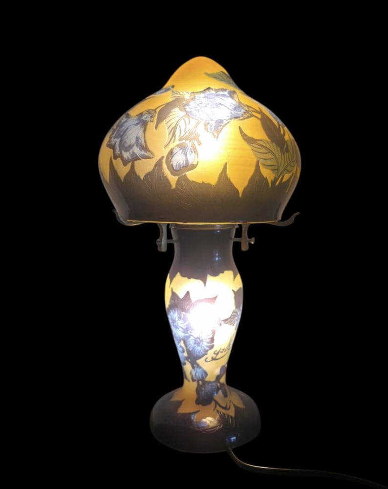 May include: A vintage table lamp with a yellow and brown glass shade featuring blue floral designs. The lamp has a curved base and a slender stem, with a black power cord.