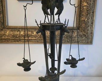 May include: An antique bronze candelabra with a detailed design. The candelabra features three bird figures at the top, deer heads, and hanging oil lamps. The base has a decorative, ornate design. The overall color is dark bronze.