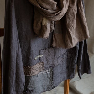 Puede incluir: Una camisa de lino gris con un diseño de patchwork y una bufanda de lino marrón. La camisa tiene un corte holgado y mangas largas.