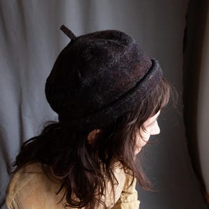 May include: A dark brown and grey wool beret with a pointed top. The beret is worn on the head of a person with long brown hair.