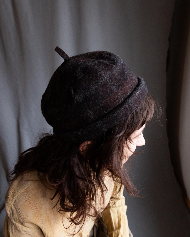 May include: A dark brown and grey wool beret with a pointed top. The beret is worn on the head of a person with long brown hair.