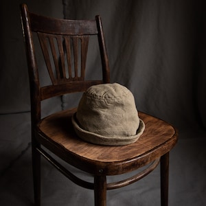 May include: A brown wooden chair with a worn, light brown fabric hat sitting on the seat.