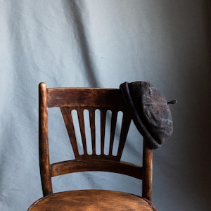 May include: A wooden chair with a dark brown finish and a slatted back. A grey felt hat is resting on the top of the chair back.