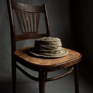 May include: A brown wooden chair with a worn, light brown seat. A light brown, fabric hat sits on the seat.