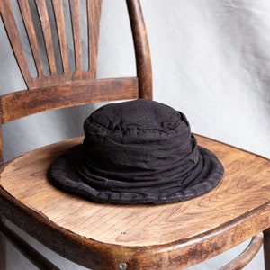 May include: A black, fabric bucket hat with a wide brim sits on a wooden chair.