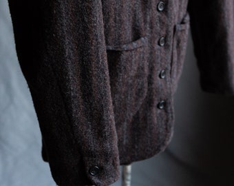 May include: A brown and black striped wool jacket with a button front and a single patch pocket on the left side. The jacket has a long sleeve with a button cuff.