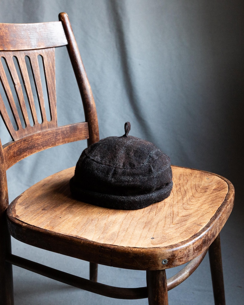 May include: A dark brown felt hat with a rounded crown and a small, pointed top sits on a wooden chair.