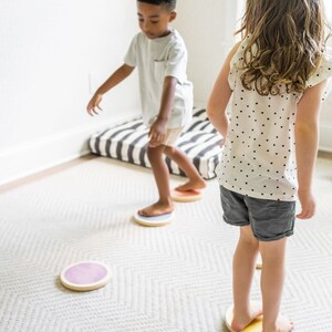 A dark-skinned boy with black hair and a light-skinned girl with brown hair playing on the stepping stones in a gray-carpeted living room.
