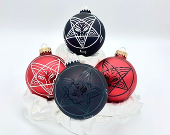 May include: Three Christmas ornaments with a pentagram design. Two are red with white pentagrams and one is black with a white pentagram.