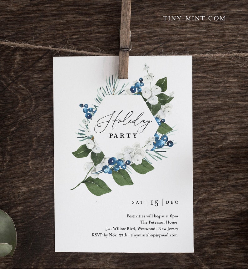 K&ouml;nnte beinhalten: Eine wei&szlig;e Einladungskarte f&uuml;r eine Weihnachtsfeier, gehalten von einer Holzklammer. Die Karte zeigt ein Aquarelldesign eines floralen Kranzes mit blauen Beeren und wei&szlig;en Bl&uuml;ten. Der Text "Holiday PARTY" ist in eleganter Schrift dargestellt.