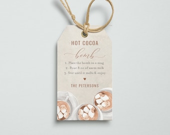 May include: A beige gift tag with a brown string, featuring the text "HOT COCOA bomb". Instructions are listed below the title. The bottom of the tag shows three watercolor illustrations of mugs of hot cocoa with marshmallows. The website TINY-MINT.COM is at the bottom.
