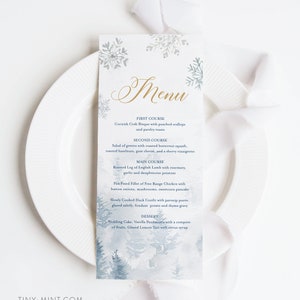 Peut inclure: Une carte de menu sur le thème de l'hiver, avec une illustration à l'aquarelle d'une forêt enneigée et de flocons de neige. Le mot "Menu" est en écriture dorée. Le menu propose un repas en plusieurs services, dont une bisque de crabe et une cuisse d'agneau rôtie.