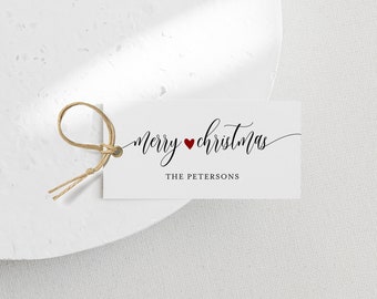Può includere: Un'etichetta regalo bianca con le parole "merry christmas" in elegante scrittura nera, un cuore rosso e "THE PETERSONS" sotto. Un anello di spago naturale è attaccato all'etichetta.