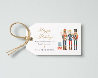 Può includere: Un'etichetta regalo bianca con la scritta "Happy Holidays" in oro. L'etichetta presenta illustrazioni di schiaccianoci e un re topo. Un cordino di spago è attaccato all'etichetta.