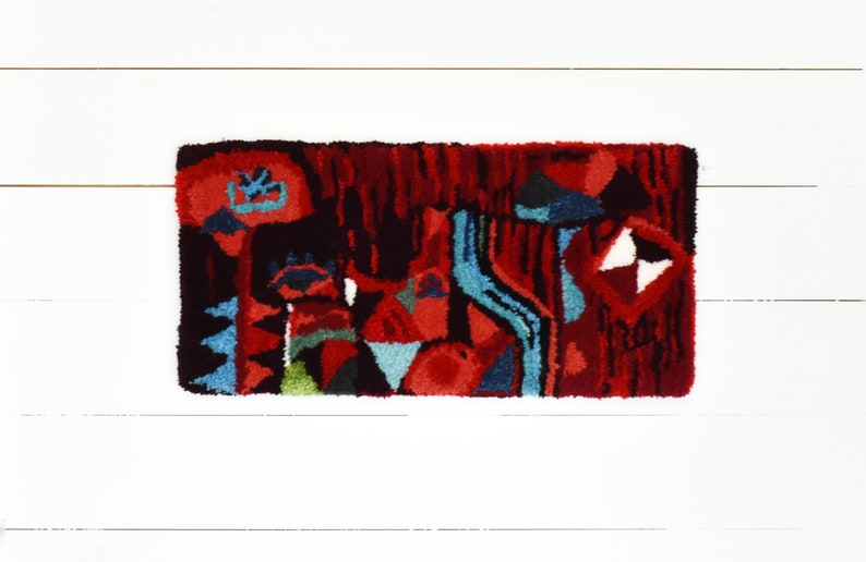 Puede incluir: Una alfombra abstracta colorida con un dise&ntilde;o rojo, azul, verde y negro. La alfombra est&aacute; hecha de un material grueso y texturizado y tiene un patr&oacute;n geom&eacute;trico.
