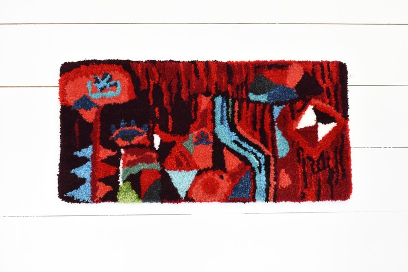 Puede incluir: Una alfombra abstracta colorida con un dise&ntilde;o rojo, azul y verde. La alfombra est&aacute; hecha de un material grueso y texturizado y tiene un patr&oacute;n geom&eacute;trico.