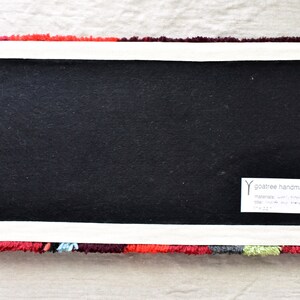 Puede incluir: La parte posterior de una alfombra colorida con un respaldo negro y una etiqueta blanca que dice "goaree handmade" con el texto "materials: wool, cotton, jute, satin, silk, viscose, soy silk" y "size: 17" x 24"  approx.  goaree.com"
