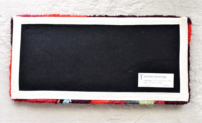 Puede incluir: La parte posterior de una alfombra colorida con un respaldo negro y una etiqueta blanca que dice "goaree handmade" con el texto "materials: wool, cotton, jute, satin, silk, viscose, soy silk" y "size: 17" x 24"  approx.  goaree.com"