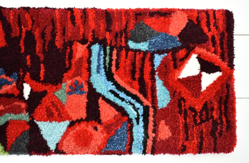 Puede incluir: Alfombra abstracta con un esquema de color rojo, azul y blanco. La alfombra tiene un aspecto texturizado y tejido a mano.