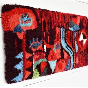 Puede incluir: Una alfombra abstracta colorida con un dise&ntilde;o geom&eacute;trico en tonos rojos, azules, verdes y negros. La alfombra est&aacute; hecha de hilo grueso y texturizado y tiene un aspecto &uacute;nico y artesanal.