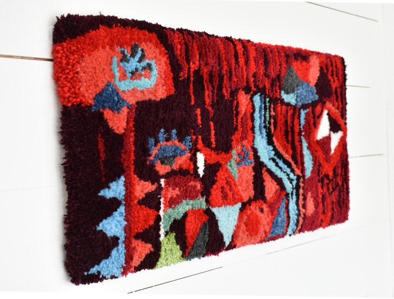 Puede incluir: Una alfombra abstracta colorida con un dise&ntilde;o geom&eacute;trico en tonos rojos, azules, verdes y negros. La alfombra est&aacute; hecha de hilo grueso y texturizado y tiene un aspecto &uacute;nico y artesanal.