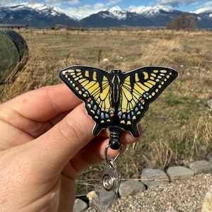 May include: A black and yellow butterfly badge reel with a clear plastic badge holder. The butterfly has black wings with yellow stripes and blue accents.