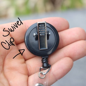 May include: Black retractable badge reel with a swivel clip. The clip is silver and has a textured surface. The reel has a clear plastic badge holder.