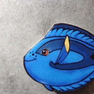 May include: A blue and yellow cartoon fish with a black outline and a white eye. The fish is smiling and has a yellow fin.