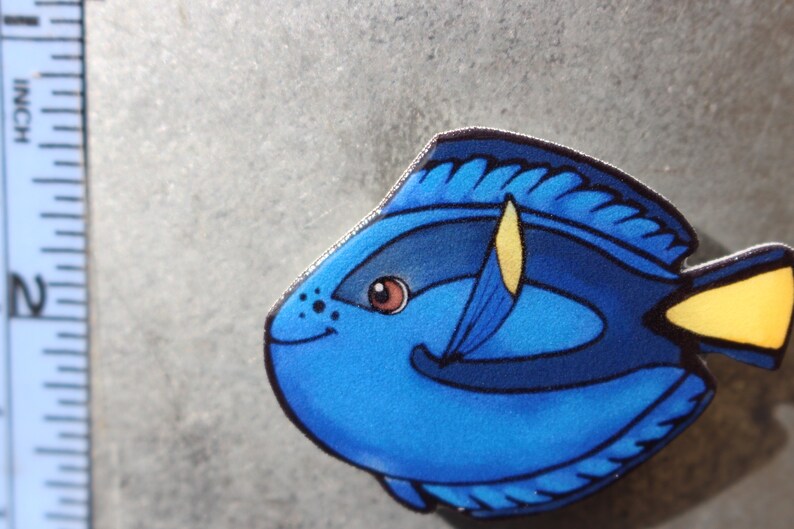 May include: A blue and yellow cartoon fish with a black outline and a white eye. The fish is smiling and has a yellow fin.