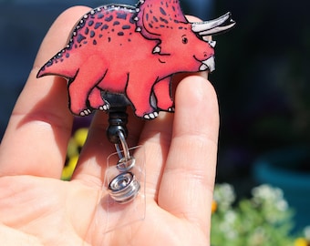 May include: A pink and black triceratops dinosaur badge reel with a silver retractable badge holder.