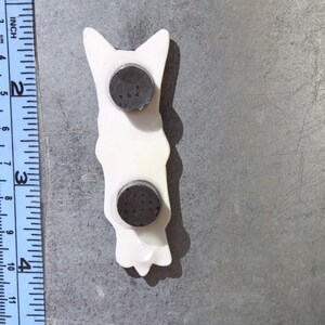 May include: White ceramic figurine of a dog with two black magnetic discs on the back.