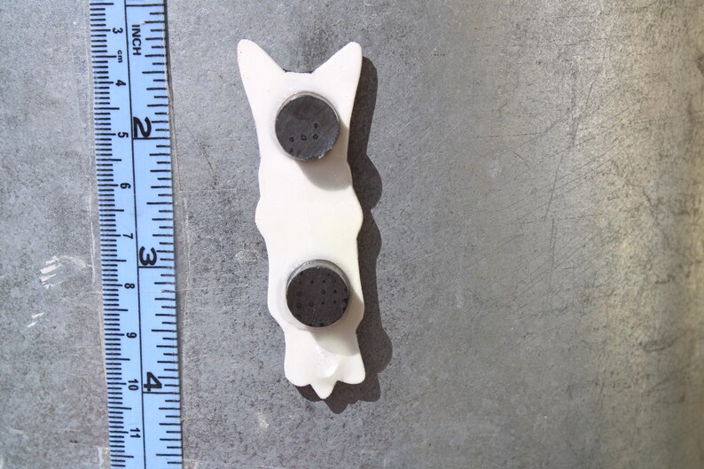 May include: White ceramic figurine of a dog with two black magnetic discs on the back.