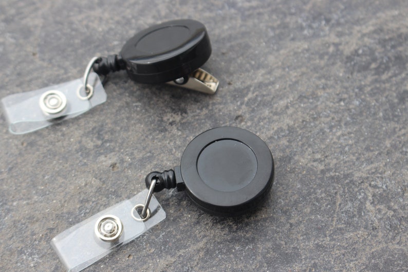 May include: Two black retractable badge holders with clear plastic badge clips. The badge holders have a metal clip on one side and a retractable cord on the other.