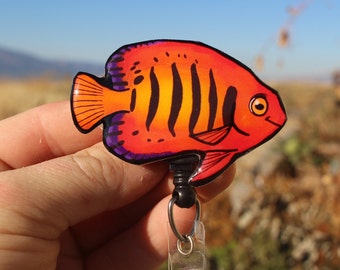 May include: A red and orange fish with black stripes and purple accents on a retractable badge reel.