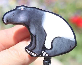 May include: A black and white cartoon tapir with a pink nose, sitting on a black retractable badge reel.