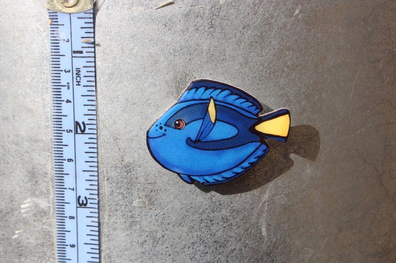 May include: A blue and yellow painted wooden fish figurine. The fish has a black eye and a yellow fin. The fish is about 2 inches long.