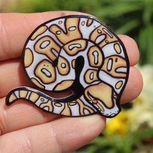 May include: A white and yellow patterned snake curled up in a coil. The snake has black eyes and a black outline.