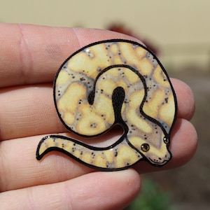 May include: A yellow and black patterned snake curled up in a coil. The snake has a glossy finish and is made of resin.
