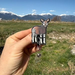 May include: A black and white striped Okapi animal badge reel with a clear plastic retractable badge holder. The badge reel is attached to a black and white striped Okapi animal charm.