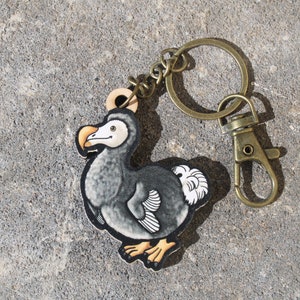 May include: A gray and white wooden dodo bird keychain with a gold metal key ring and clasp.